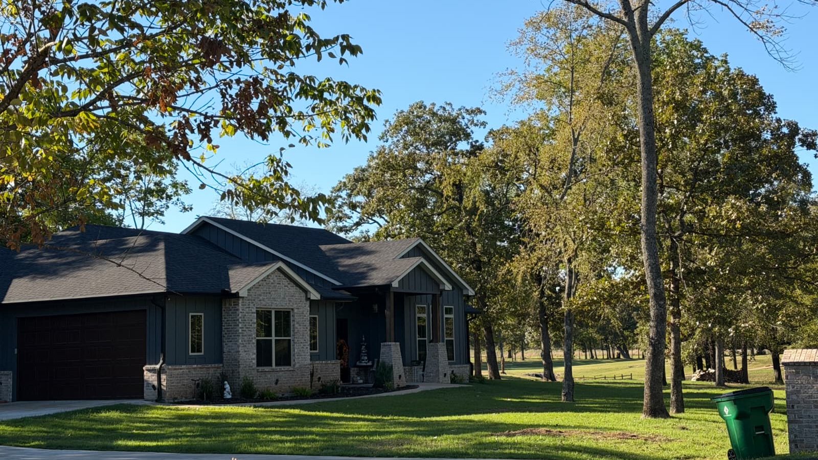 A house on a tree-lined lawn on a sunny day, with a tall bare tree in the yard